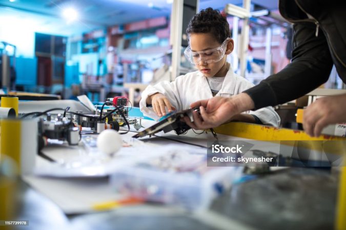 Small black engineer repairing computer motherboard with his unrecognizable teacher in laboratory.