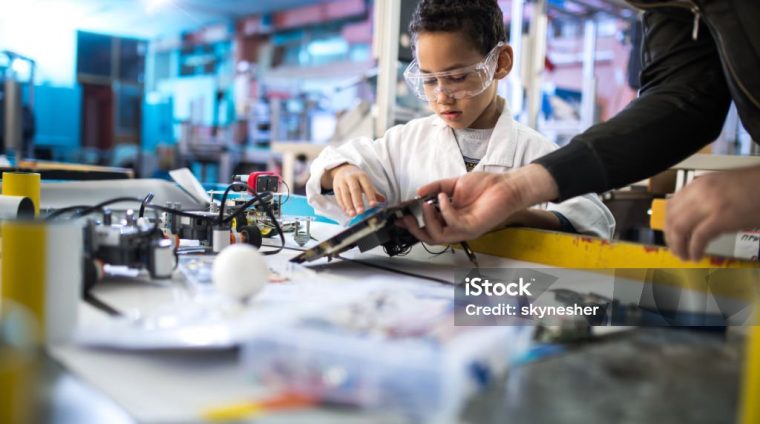 Small black engineer repairing computer motherboard with his unrecognizable teacher in laboratory.