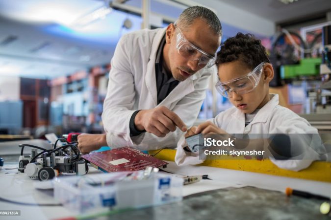Mid adult teacher and small black boy cooperating while working in laboratory.