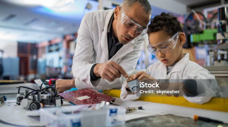 Mid adult teacher and small black boy cooperating while working in laboratory.