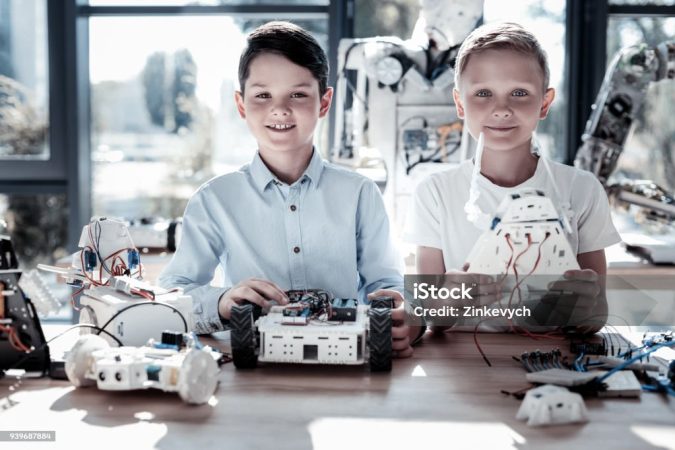 Innovative generation. Waist up shot of smart kids looking into the camera with cheerful smiles on their faces while posing with their self automated robots in hands.